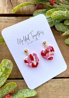 a pair of pink and red earrings sitting on top of a wooden table next to plants