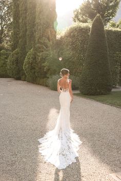 a bride and groom standing in front of some hedges at their outdoor wedding venue, with the sun shining on them