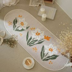 a bathroom rug with flowers on it next to a coffee cup and some other items