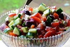 a salad with cucumbers, tomatoes, olives and feta cheese in a glass bowl