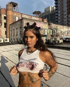 a woman with tattoos on her body standing in front of an old factory building and looking at the camera