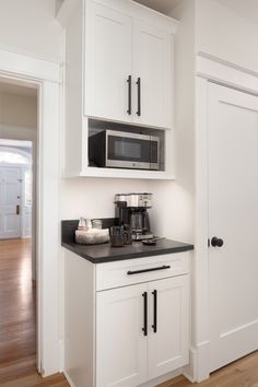 a kitchen with white cabinets and black counter tops in front of a door that leads to another room