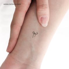 a small tattoo on the wrist of a woman's left hand, with a bow