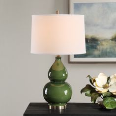 a green lamp sitting on top of a table next to a vase with white flowers