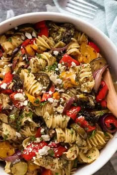 a white bowl filled with pasta salad on top of a blue towel next to a wooden spoon