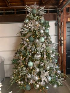 a christmas tree with ornaments and lights in a room next to a garage door,