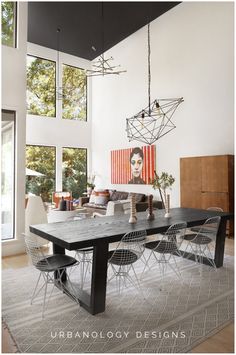 a dining room table and chairs in front of a large window with an art work on the wall