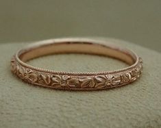 a close up of a wedding band on a cushioned surface, with flowers and leaves engraved on the side