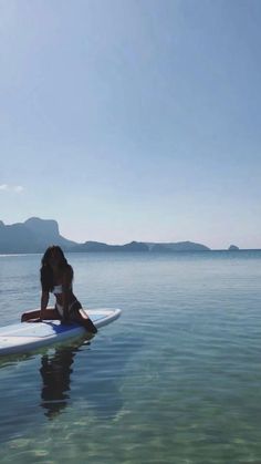 a woman is sitting on a surfboard in the water with mountains in the background