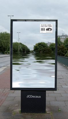 a large mirror sitting on the side of a road next to a street sign and trees