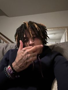 a man with dreadlocks is sitting on a couch and making a hand gesture