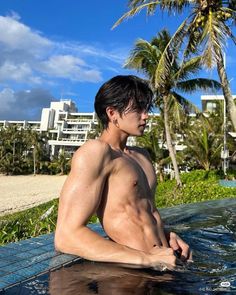 a shirtless man sitting in the middle of a pool with palm trees behind him