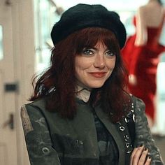 a woman with red hair wearing a black hat and green jacket standing in front of mannequins