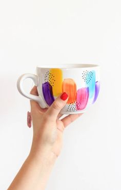 a hand holding a coffee cup with colorful paint on it's sides and the inside