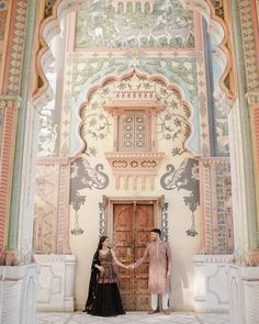 two women standing next to each other in front of a building with painted walls and doors