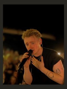 a man holding a microphone in his right hand and wearing a black shirt with tattoos on it