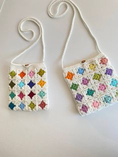 two crocheted purses are sitting on a white surface, one is multicolored