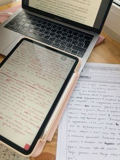 an open laptop computer sitting on top of a wooden desk next to a paper and pen