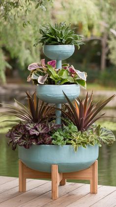 three tiered planter with plants in it sitting on a wooden deck next to water