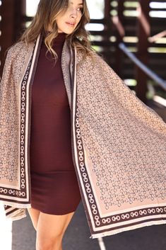 a woman is walking down the street wearing a brown dress and a beige shawl