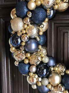 a wreath made out of ornaments hanging on the front door with gold, black and silver balls