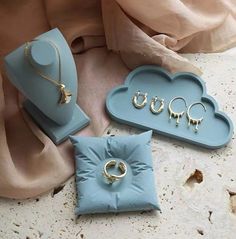 three pieces of jewelry sitting on top of a blue tray next to a pink scarf