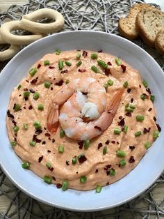 a white bowl filled with hummus and shrimp on top of a table next to crackers