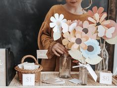 a woman arranging flowers in a vase on a table with cards and tags around it