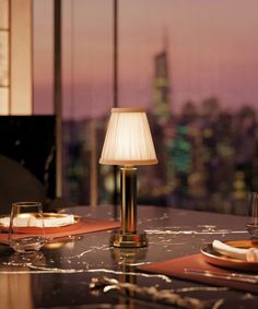 a table with plates, glasses and a lamp on it in front of a cityscape