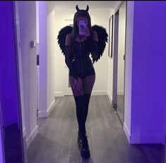 a woman in a devil costume is taking a selfie with her cell phone while walking down the hall way