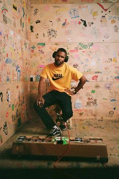 a man sitting on top of a piece of luggage in front of a wall covered with stickers