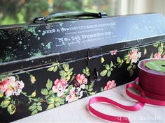 a black box with flowers on it next to a pink ribbon and a pair of scissors