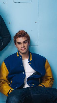 two young men sitting next to each other in front of a blue and yellow wall