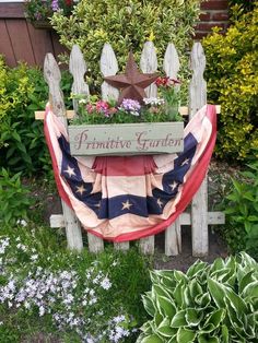 a wooden bench with an american flag draped over it in front of some flowers and plants