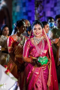 a woman in a pink and gold sari is walking down the aisle with other people