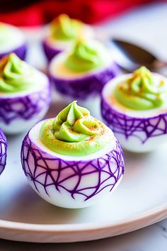 small cupcakes decorated with green and purple icing on a white platter