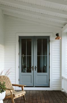 a wooden chair sitting on top of a porch next to a blue front door with two glass doors