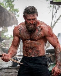 a shirtless man holding a knife and looking at the camera with blood all over his body