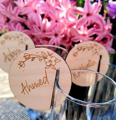 three wooden name tags sitting on top of glass vases filled with pink and purple flowers