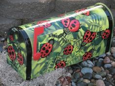 a painted mailbox with ladybugs on it sitting next to some rocks and grass