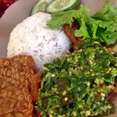 a plate filled with rice, meat and veggies next to cucumbers