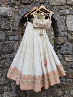 This stunning ivory Lucknowi thread work georgette lehenga is embellished with heavy gota, sequin, pearl and zari work border in pink accent. It is paired with a bustier in raw silk with mirror, zardozi and thread zardozi work all over.  The outfit is completed with a pink net dupatta with mirror work highlights. Ivory Lehenga Simple, White And Peach Lehenga, Ivory Mirror Work Lehenga, Cute Indian Outfits, Lucknowi Lengha, Off White Raw Silk Lehenga For Reception, Traditional Drape Raw Silk Lehenga With Pearl Embroidery, Cream Choli With Pearl Embroidery And Traditional Drape, Fitted Beige Georgette Lehenga