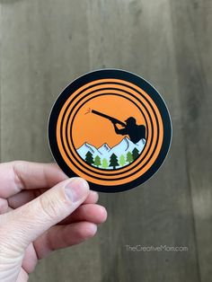 a hand holding an orange and black sticker with a mountain scene in the center