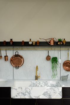 a kitchen with marble counter tops and copper pots hanging on the wall above the sink