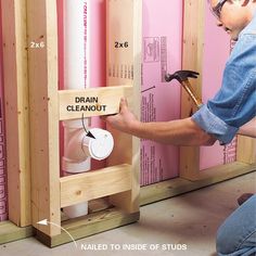 a man working on a wall with pink walls and wooden framing around it that says drain cleanout, nailed to inside of studs