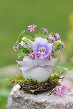 a white egg with purple flowers in it sitting on a rock next to grass and flowers