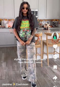 a woman standing in a kitchen with her hands on her hips and wearing camouflage pants