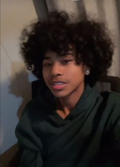 a woman with curly hair sitting in a chair and looking at the camera while wearing a green shirt