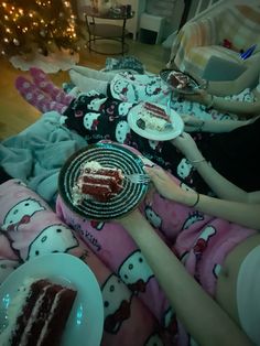 two women sitting on the floor with plates of cake in front of them and a christmas tree behind them