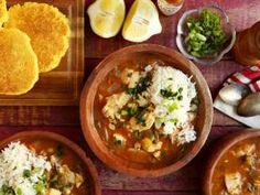 three bowls filled with different types of food on top of a wooden table next to bread